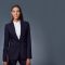 Smiling young female professional standing against gray background. Portrait of beautiful businesswoman holding document. She is blue suit.